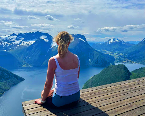 Kvinne sitter på et utkikkspunkt og ser utover fjord og fjell