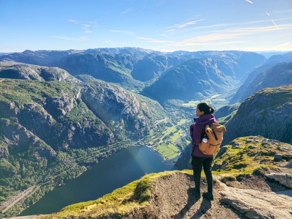 A traveler gazes at the stunning fjord landscape, bathed in early morning light, surrounded by towering mountains and lush valleys. Lysefjord Kjeragbolten Norway