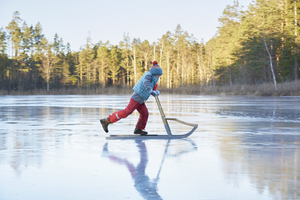 Boy skating on sleigh across frozen lake