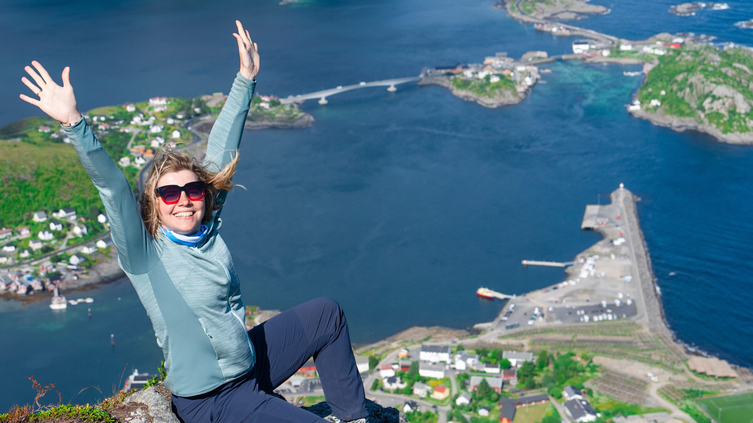 Happy woman hiker enjoys the panorama of lofoten islands at the top of Reinebringen. traveler alone on cliff edge in Norway lifestyle exploring concept. Hike above Reine village in the Lofoten archipelago, travel to Norway