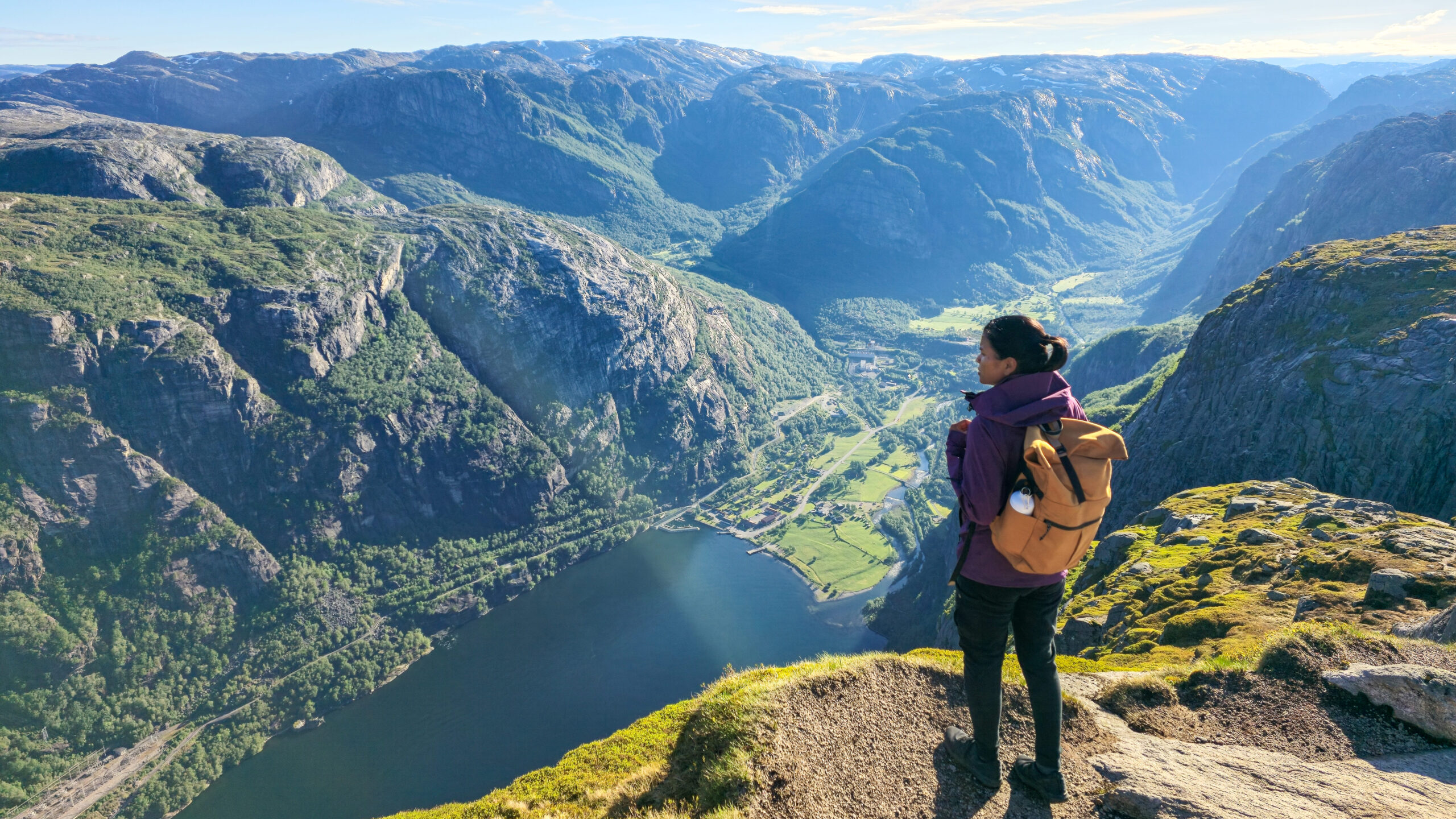 A traveler gazes at the stunning fjord landscape, bathed in early morning light, surrounded by towering mountains and lush valleys. Lysefjord Kjeragbolten Norway