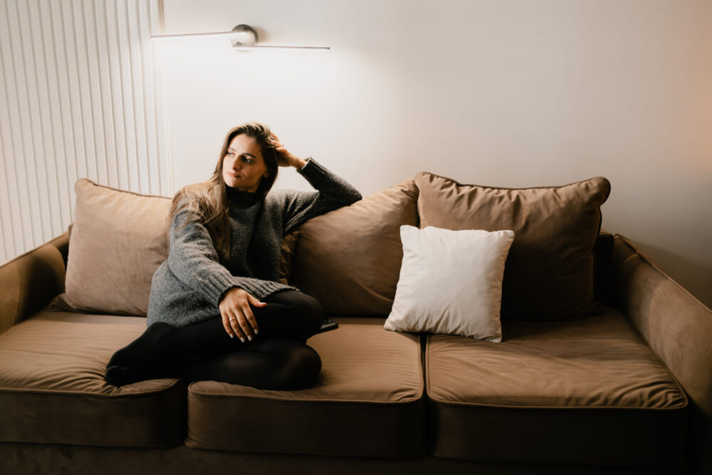 A woman comfortably seated in a warm and cozy environment with contemporary decor, exuding a sense of relaxation. The soft lighting enhances the serene atmosphere of the interior living space.