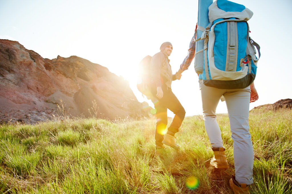 Young man holding his girlfriend by hand while walking on grass on sunny day