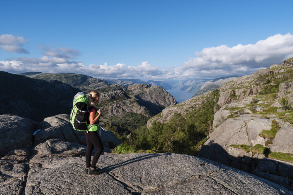 Tourist with a backpack on pathway Pulpit Rock. Blond girl in a mountain trek. View of Lysefjord, Norway
