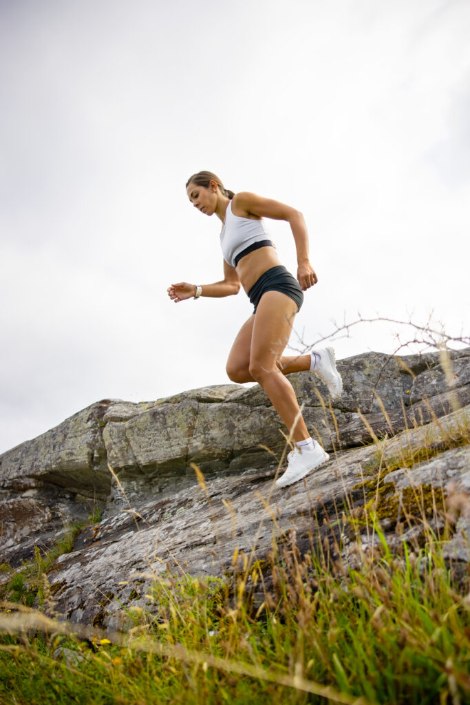 Side view of fitness woman running high-intensity interval training on a steep hill up a mountain. HILIT workout.
