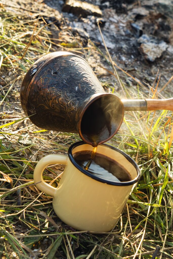 Yellow metal cup with hot coffee and cezve on a grass on the background of bonfire.