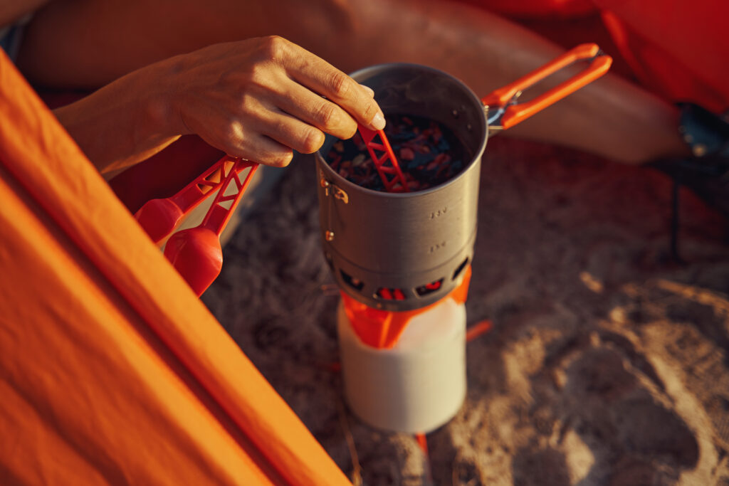 Person using orange spoon fork knife set and stirring herbal tea in mug, standing on gas burner